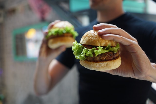 hamburger, muž jej drží v ruce a v druhé taky